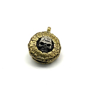 May include: A gold-toned pendant with a silver skull in the center. The skull has Roman numerals on its forehead and is surrounded by a circle of smaller skulls.