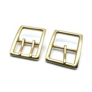 Può includere: Due fibbie per cintura in metallo dorato di forma quadrata con un design a doppia linguetta.