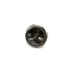 May include: A silver bottle stopper with a detailed, textured design. The stopper has a circular base with a central hole and a decorative top. The design appears to be of a mythical creature or animal.