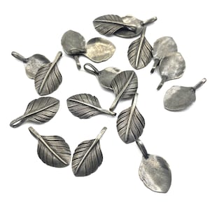 Op de afbeelding: Een verzameling van 14 zilverkleurige verencharms met een textuur. De charms zijn verspreid over een witte achtergrond.