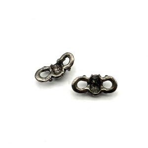 May include: Two antique silver-toned metal clasps. Each clasp has a decorative design with a central element and two looped ends. The clasps are displayed on a white background.
