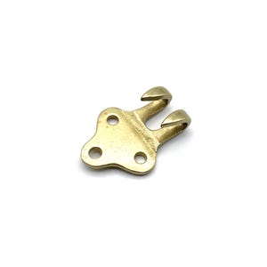 May include: A gold-toned metal hook with two prongs and a flat base with three holes.
