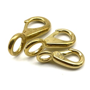 Puede incluir: Tres mosquetones de metal de color dorado de diferentes tamaños. Los mosquetones están todos cerrados y tienen un acabado liso y pulido.