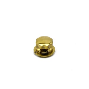 Puede incluir: Un pomo de metal dorado con una parte superior acanalada y una base circular.