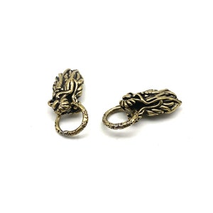May include: Two gold-toned metal dragon head belt buckles with ornate details. Each buckle has a ring for attaching to a belt.