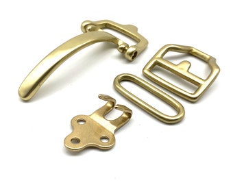 May include: A set of four brass belt buckle hardware pieces. The set includes a buckle, a keeper, a hook, and a strap end. The pieces are all made of polished brass and have a shiny finish.