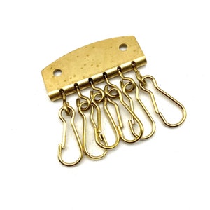 以下が含まれることがあります： 6つの回転式フックが付いた金色の金属製のキーホルダー。キーホルダーは、2つの穴のある長方形のベースを持っています。