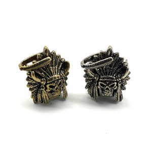 May include: Two metal skull head charms with a Native American headdress design. One charm is gold and the other is silver.