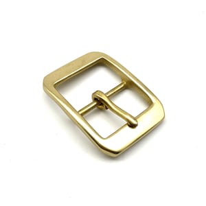 May include: A gold-toned metal buckle with a square shape and a smooth finish. The buckle has a single prong for attaching to a strap.
