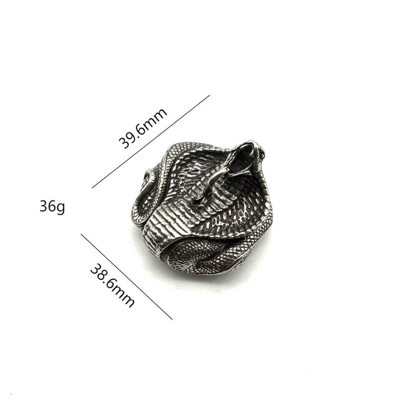 May include: A silver-coloured ring in the shape of a cobra. The ring measures 39.6mm long, 38.6mm wide, and weighs 36g. The cobra is coiled with its hood raised and mouth open. The ring has a detailed, textured surface.