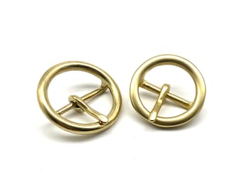 May include: Two gold-toned metal belt buckles with a round, circular design. The buckles have a centre bar that is perpendicular to the circle.