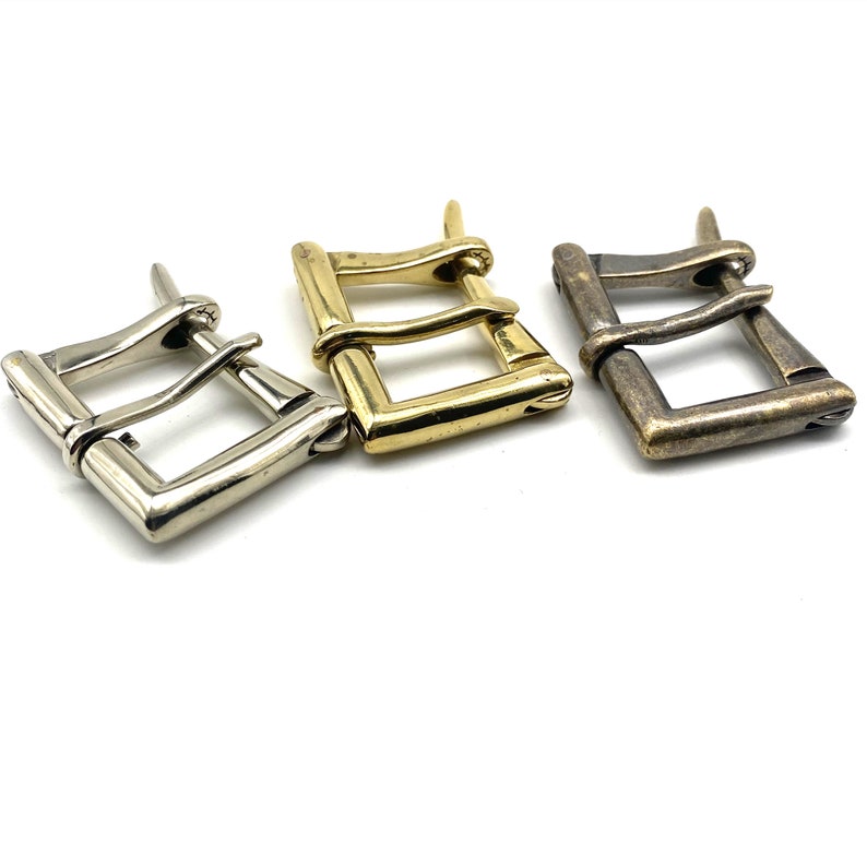 May include: Three metal belt buckles in different finishes: silver, gold, and antique brass. Each buckle has a rectangular shape with a double-prong design.