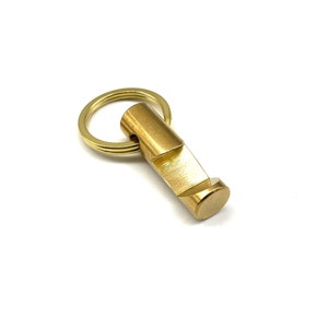 Op de afbeelding: Een gouden flesopener met een sleutelhanger. De opener heeft een gladde, geborstelde afwerking.