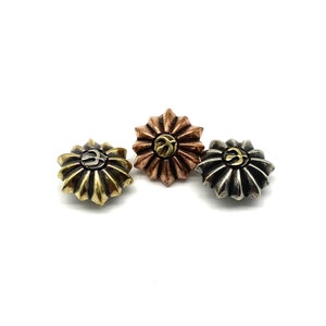Op de afbeelding: Drie decoratieve metalen knopen met een bloemvormig ontwerp. De knopen zijn in goud, koper en zilver tinten. Elke knop heeft een verhoogd symbool in het midden.