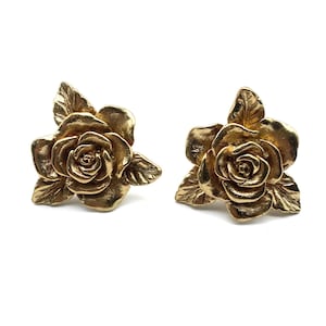 Könnte beinhalten: Ein Paar goldfarbene Rosenblüten-Ohrstecker. Die Ohrringe sind aus Metall und haben ein detailliertes Design.