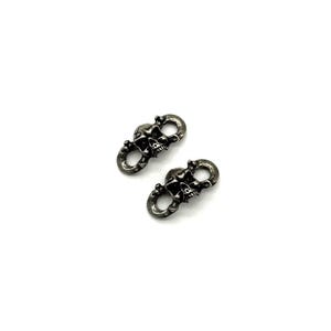 May include: Two small, silver-toned metal charms, each featuring a skull design. The skulls are detailed with visible teeth and eye sockets, connected by a loop. The charms are set against a plain white background.