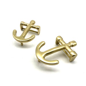 Puede incluir: Dos hebillas de cinturón de metal dorado en forma de ancla. Las hebillas están detalladas con una barra transversal y un bucle.