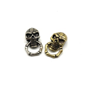 May include: Two skull-shaped keychains, one silver and one gold, with a ring attached to each skull.