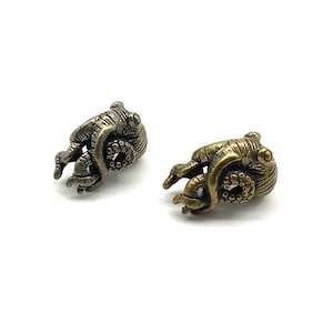 Op de afbeelding: Twee octopusvormige metalen bedels, een in zilver en een in goud. De bedels zijn gedetailleerd met getextureerde tentakels en ogen.