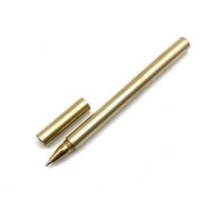 Könnte beinhalten: Ein goldfarbener Metall-Stift mit Kappe. Der Stift ist ausgefahren und die Kappe ist abgenommen. Der Stift befindet sich auf einem weißen Hintergrund.