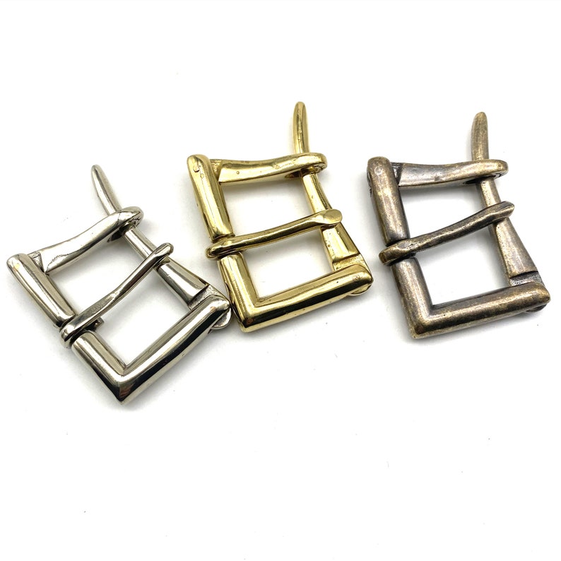May include: Three metal belt buckles in different finishes: silver, gold, and bronze. Each buckle has a rectangular shape with a double-loop design.