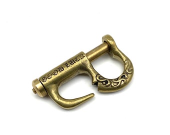 May include: A gold-toned metal hook with an ornate design and the words "GOOD LUCK" engraved on the side.