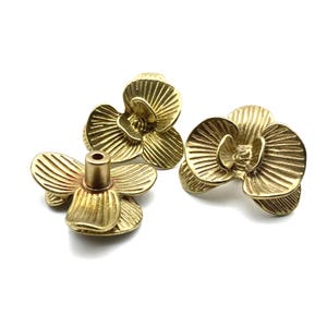 May include: Three gold metal orchid flower embellishments. Each flower has a three-dimensional design with a textured surface.