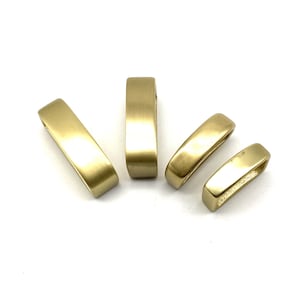 May include: Four gold-colored metal belt buckle rings. The rings are smooth and have a slightly rounded rectangular shape.
