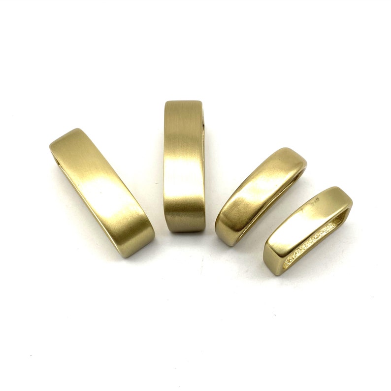 May include: Four gold-colored metal belt buckle rings. The rings are smooth and have a slightly rounded rectangular shape.