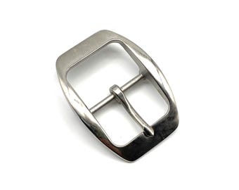 May include: A polished, silver-toned metal belt buckle. It features a rectangular frame and a central pin for securing a belt. The buckle is displayed on a white background.