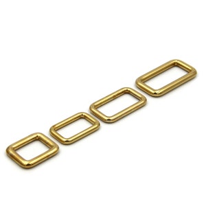 Op de afbeelding: Vier gouden metalen D-ringen in verschillende maten. De ringen zijn gerangschikt in een rij van groot naar klein.