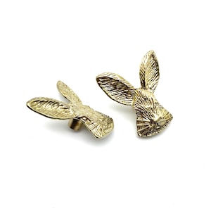 May include: Two gold-toned rabbit head drawer pulls. The rabbit's ears are long and pointed, and the face is detailed with a textured finish.