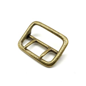May include: A gold-toned metal buckle with a textured finish. The buckle is rectangular in shape with rounded corners and a single prong.