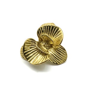 May include: A gold-colored metal flower charm with a three-dimensional design. The flower has three petals with a textured surface.