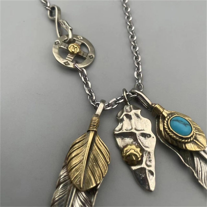 May include: Silver chain necklace with multiple charms, including three silver feathers with gold accents, a silver charm with a turquoise stone, and a silver charm with a circular design.