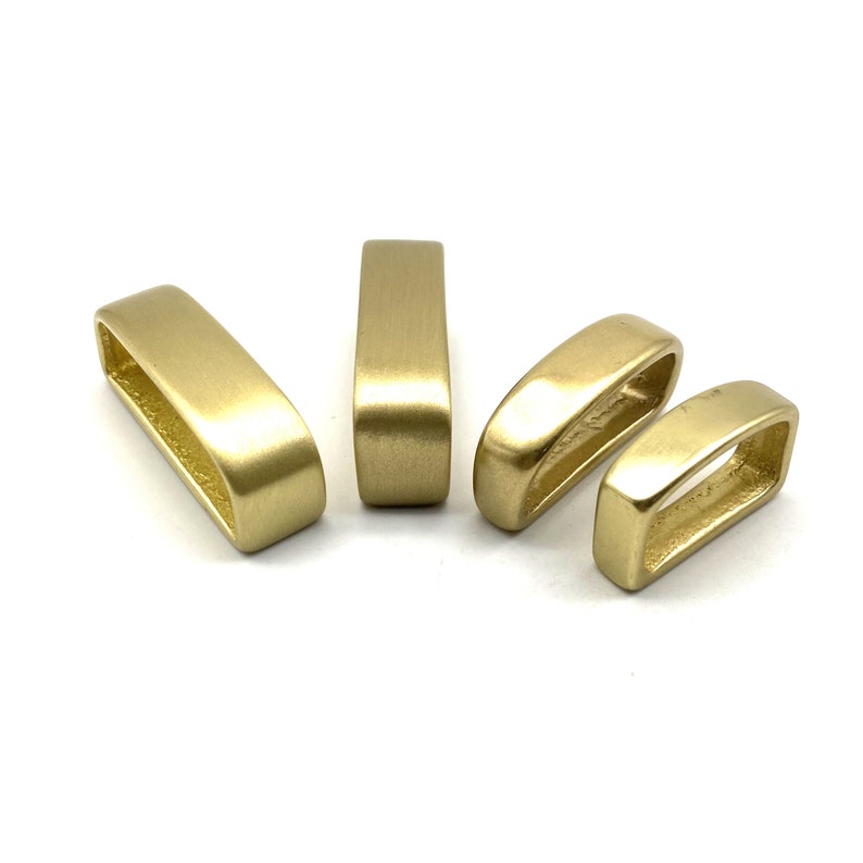 May include: Four gold-colored metal belt loops of varying sizes. The loops are smooth and have a slightly rounded edge.