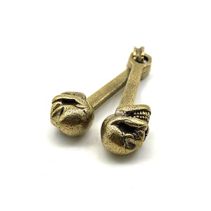 Puede incluir: Dos pendientes antiguos en forma de calavera de color latón. Cada pendiente presenta un diseño detallado de calavera en la parte inferior, conectado a una barra delgada y una parte superior hexagonal. Los pendientes tienen un aspecto texturizado y envejecido.