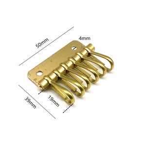 以下が含まれることがあります： 6つのフックと厚さ4mmのプレートが付いた真鍮製のキーホルダー。キーホルダーの長さは50mm、幅は39mm、高さは19mmです。