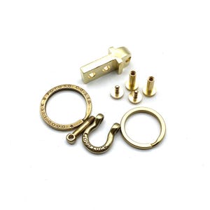 May include: A gold-toned metal key chain with a hook, a ring, and a small metal plate with the text "GOOD LUCK POTOONG CO. LTD". The key chain is disassembled and includes four small screws.