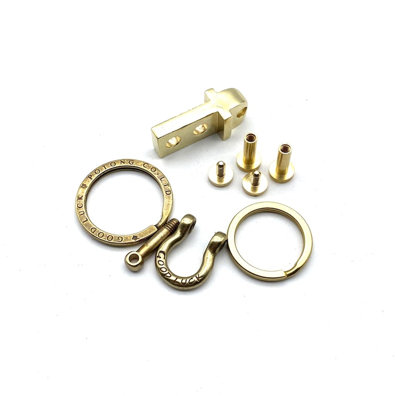 May include: A gold-toned metal key chain with a hook, a ring, and a small metal plate with the text "GOOD LUCK POTOONG CO. LTD". The key chain is disassembled and includes four small screws.