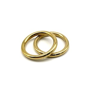 May include: Two gold-coloured metal rings, one slightly larger than the other, are interlocked.
