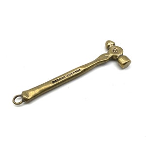 May include: A small brass hammer with a ball-peen head. The hammer has a loop at the end of the handle and the words "Becker Custom" engraved on the handle.
