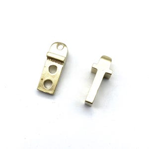 May include: Two gold metal hardware pieces for furniture. One piece is a rectangular shape with three holes and the text "PT Reinforced" on the side. The other piece is a T-shaped piece.