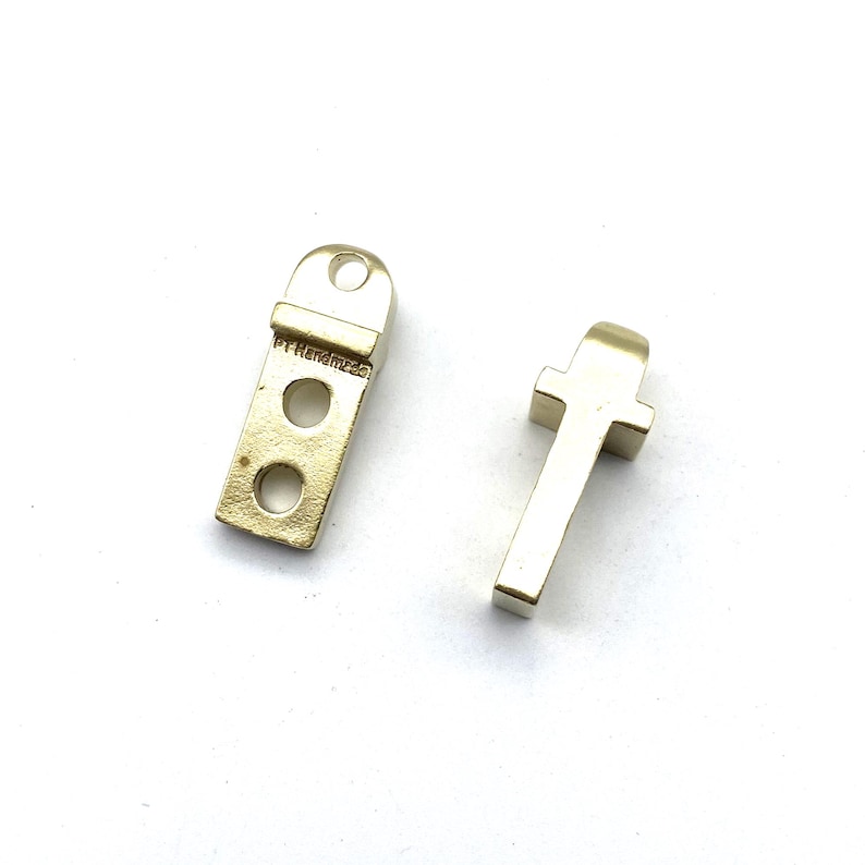 May include: Two gold metal hardware pieces for furniture. One piece is a rectangular shape with three holes and the text "PT Reinforced" on the side. The other piece is a T-shaped piece.