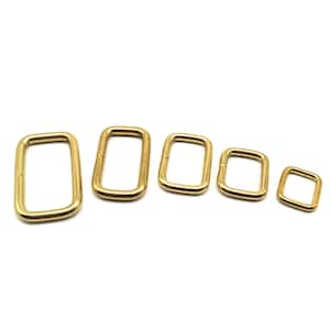Puede incluir: Cinco anillos rectangulares de metal de color dorado de diferentes tamaños. Los anillos están dispuestos en una fila del más grande al más pequeño.