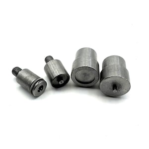 May include: Four metal snap press tools for attaching snaps to fabric. The tools are different sizes and have a silver finish.