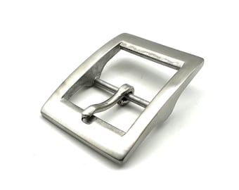 May include: A silver-coloured metal belt buckle. It has a rectangular frame and a curved, hinged pin. The buckle is designed for use with a belt and has a simple, classic design. The metal has a brushed finish.