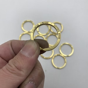 May include: A set of 10 gold-coloured key rings with the text "FIELDWORK COMPANY - LEATHER HOUSE" engraved on one of the rings.