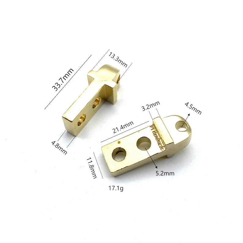 May include: Two gold-colored metal hardware pieces with holes and rounded edges. The larger piece measures 21.4 mm by 11.8 mm and weighs 17.1 g. The smaller piece measures 13.3 mm by 33.7 mm.