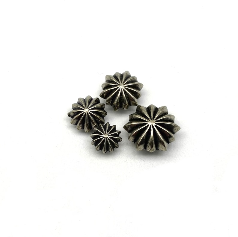 May include: Four silver star-shaped buttons of varying sizes. The buttons have a raised, textured design.